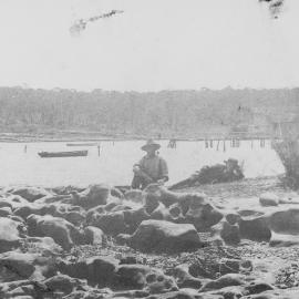 Gunnamatta Bay, view of boats on the water and two men near rocks in the foreground, ca. 1905