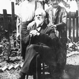 Adam Vallance seated outside with two other family members standing behind him, ca. 1900s